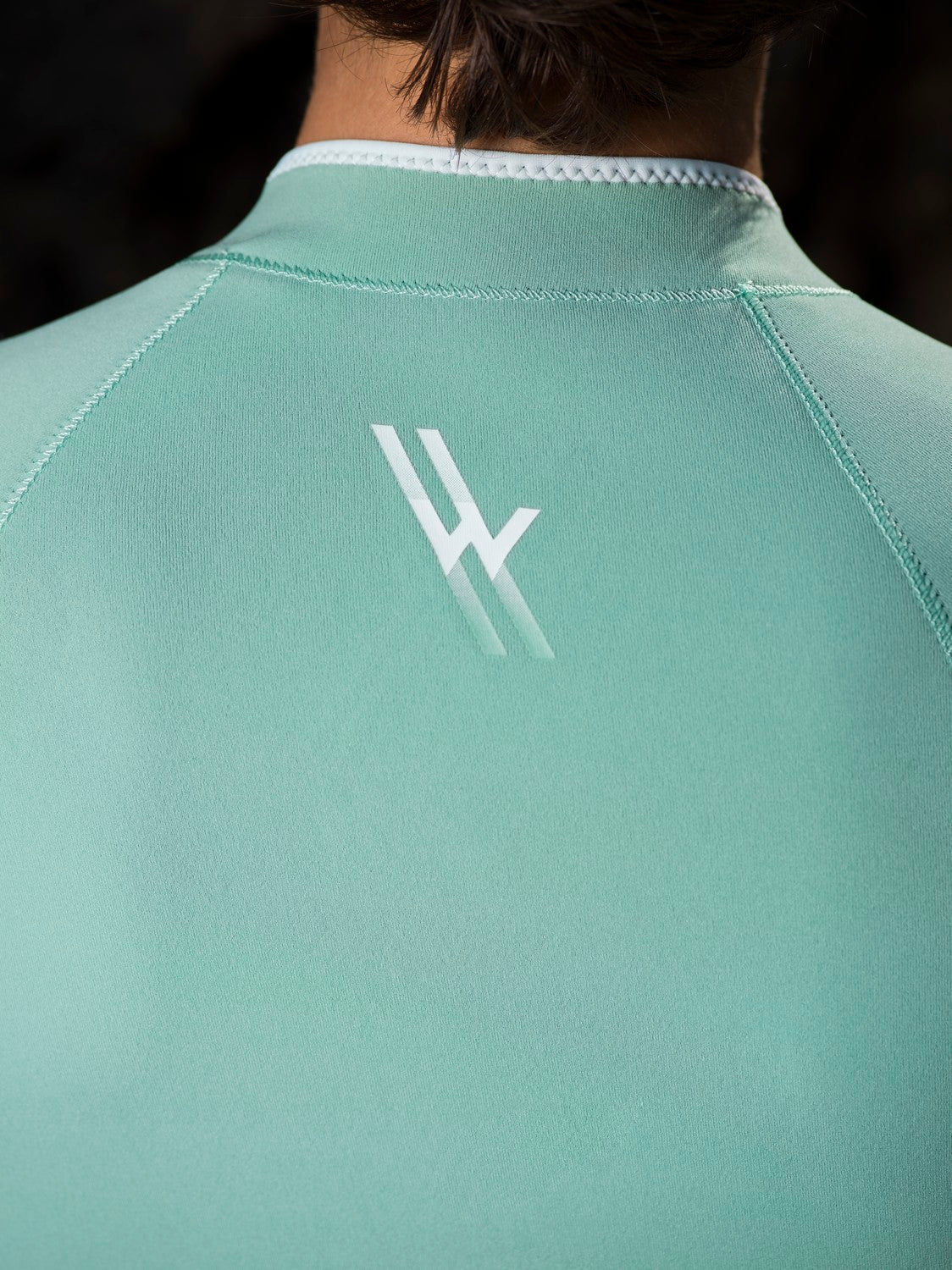 Close-up of WALLIEN logo on aquamarine Yulex® springsuit back, showing smooth, sustainable wetsuit fabric and GBS stitching