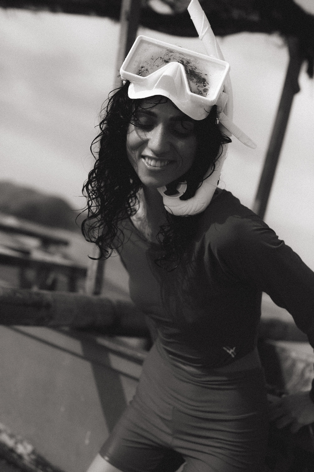 Smiling woman in teal rash guard top with snorkel mask, leaning on boat edge, monochrome seaside setting in soft focus